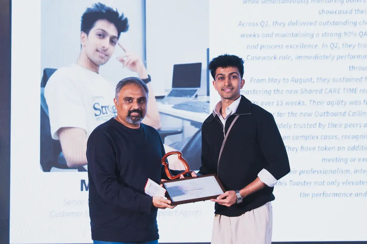 A winner collecting a trophy and certificate on stage beside their citation