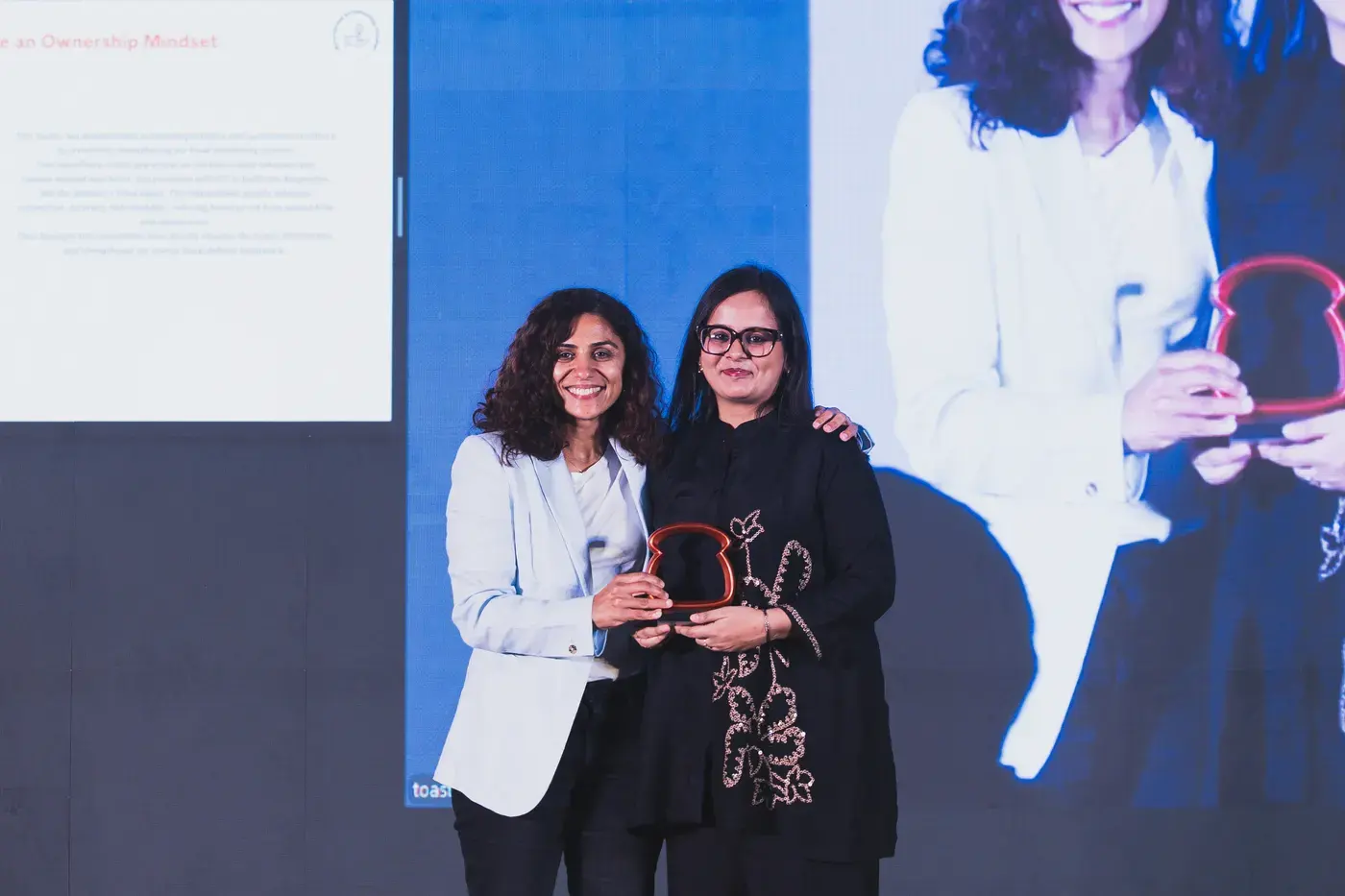 Two colleagues holding their trophies up for the camera on stage