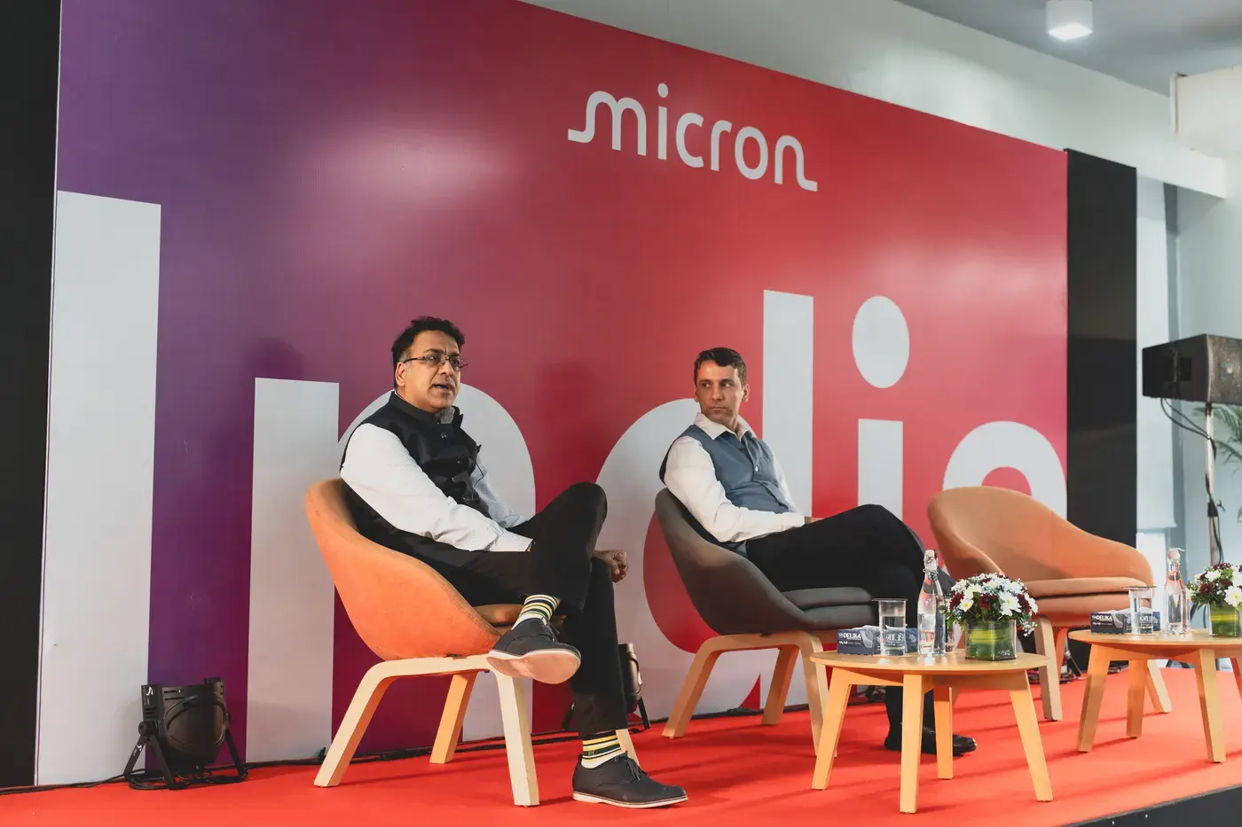 Two speakers in conversation on an orange stage against a branded backdrop