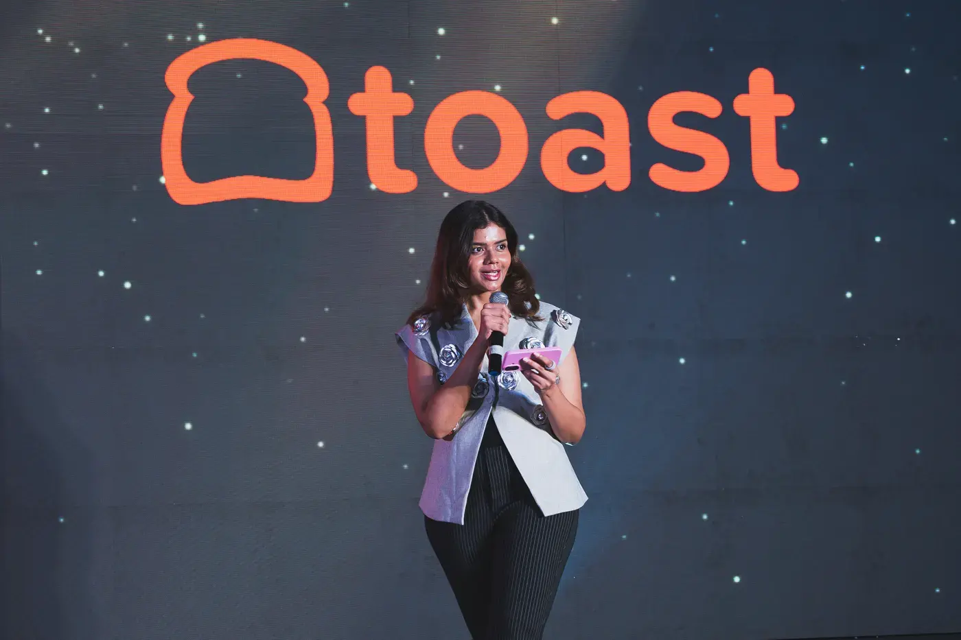A speaker addressing the room from the stage against an illuminated brand wall