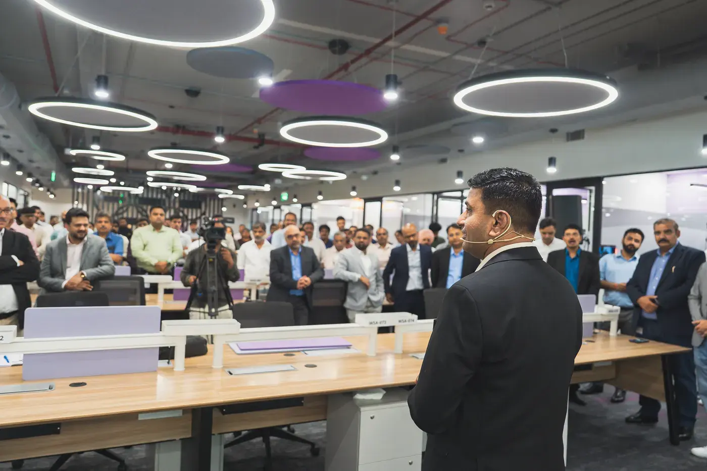 A host presenting to a standing audience across an open-plan office floor