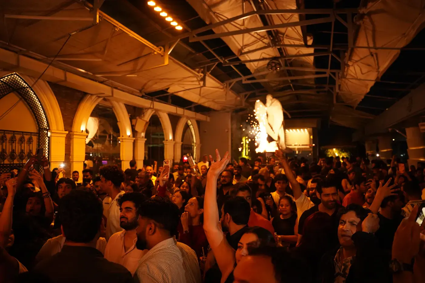 A crowd dancing with hands raised under warm light